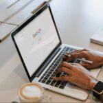 Woman wearing a watch typing on a laptop with the word “search” on the screen.