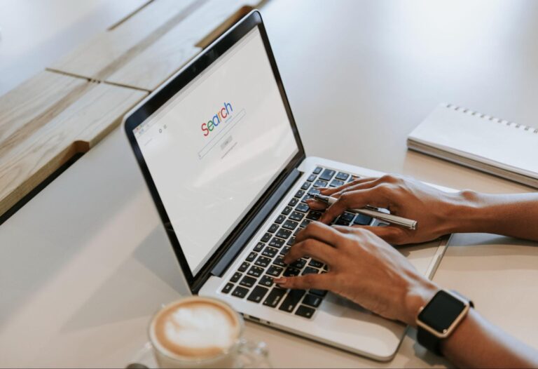 Woman wearing a watch typing on a laptop with the word “search” on the screen.