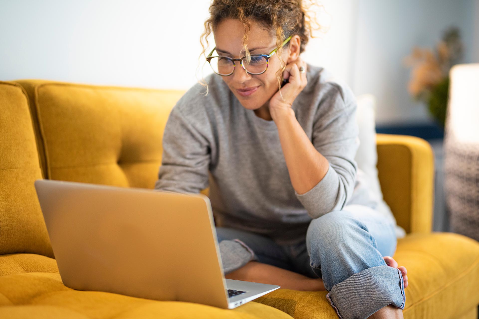 Female sitting on a yellow couch using laptop.