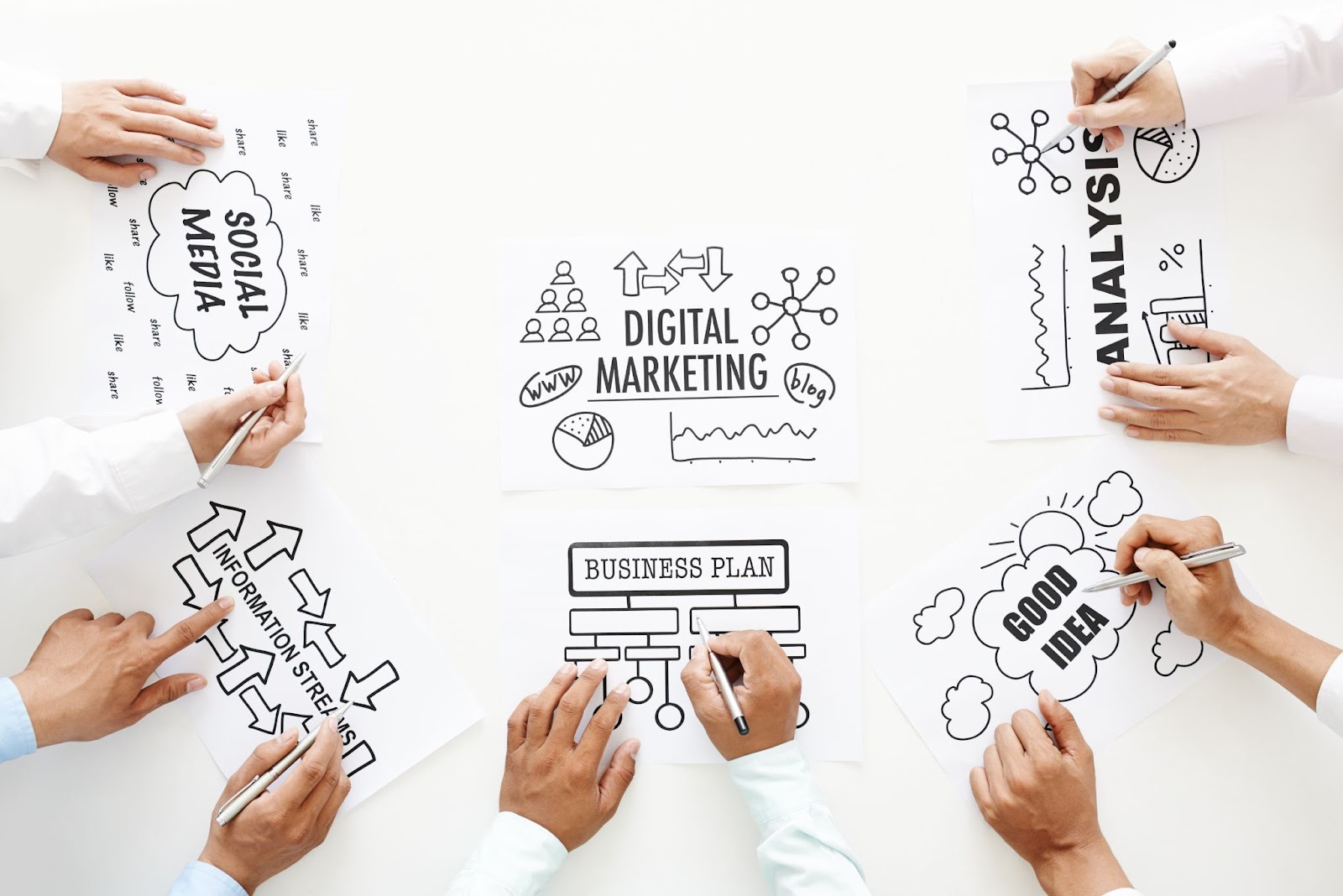 Hands holding pens, pointing at infographics printed on pieces of paper.