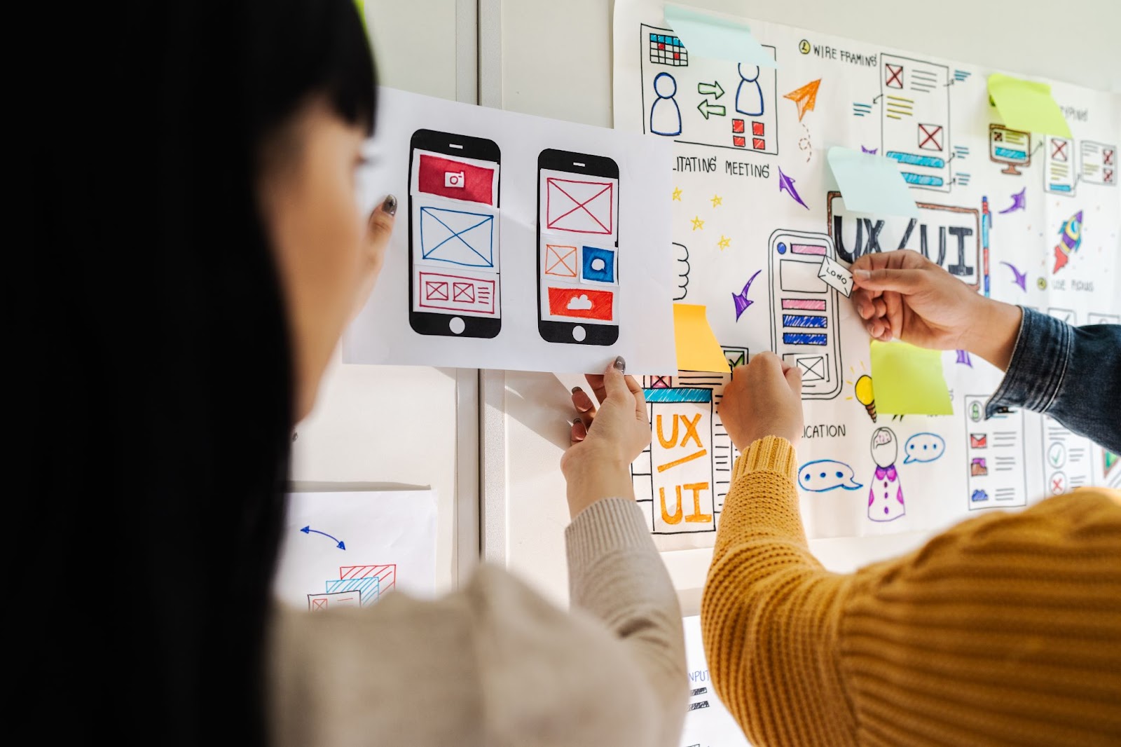 Three designers adding to a vision board with the words “UX/UI” written down.