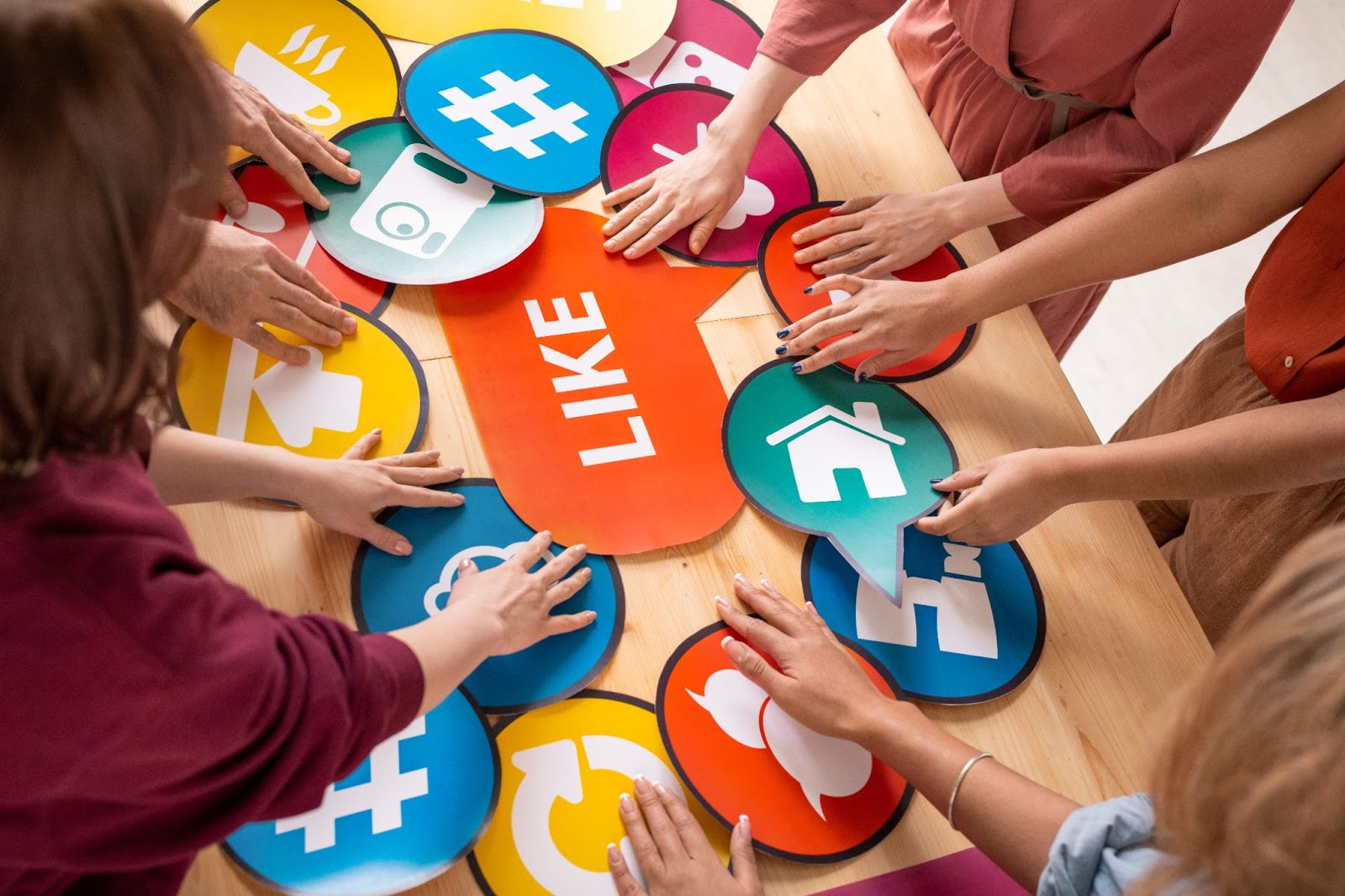 People placing their hands on social media icons on a wooden surface. 