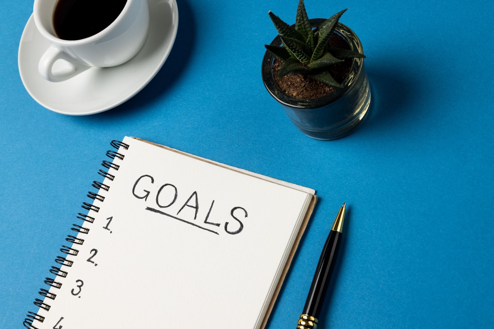 Word “goals” written on a piece of paper next to a cup of coffee and a succulent.