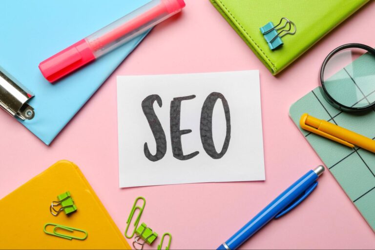 Word “SEO” written on a piece of paper next to pens, folders, and paper clips.