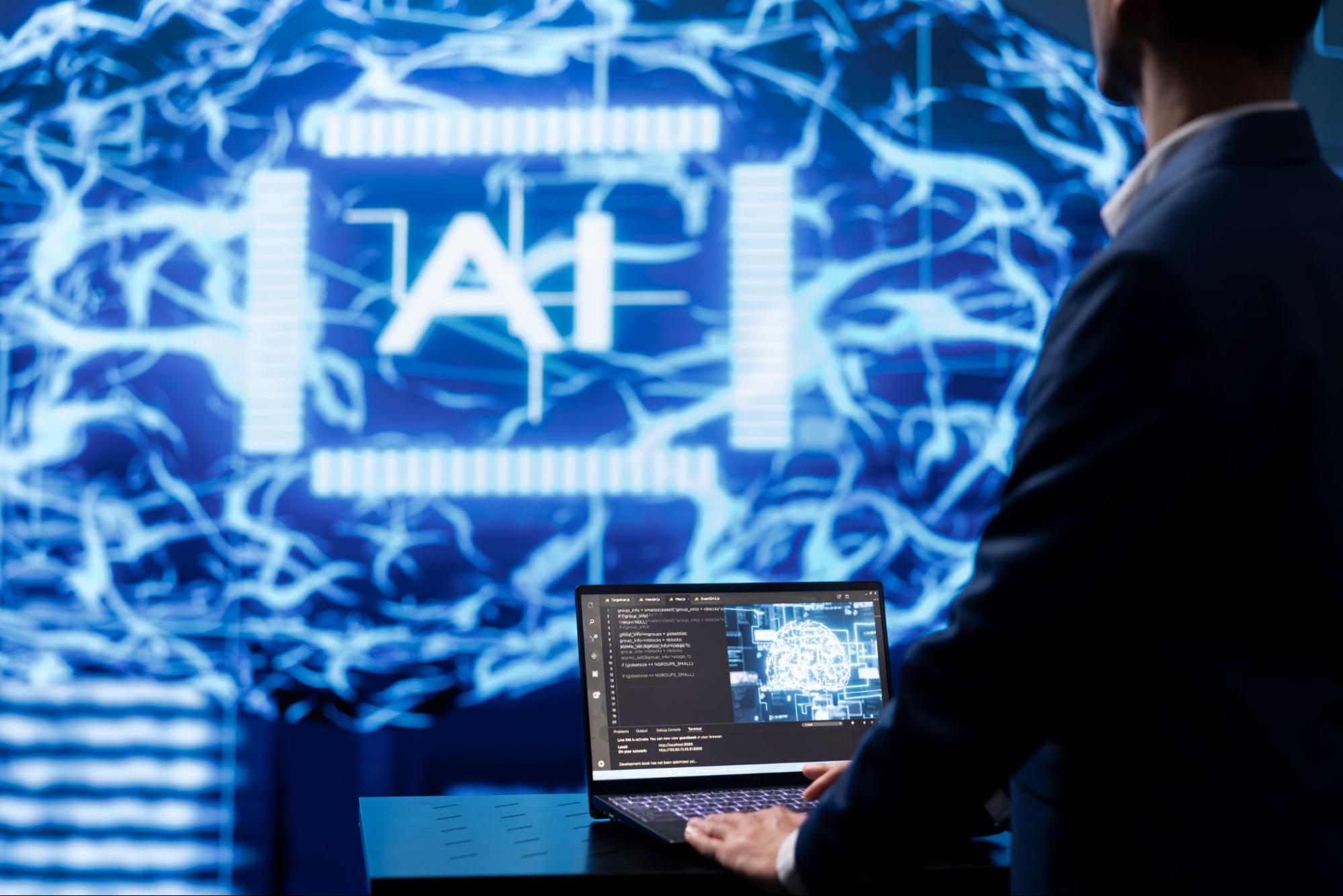 Man on a laptop next to a screen that says “AI.”