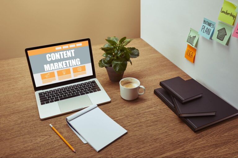 A laptop on a desk with the words content marketing displayed on the screen next to a cup of coffee, a plant, and books.