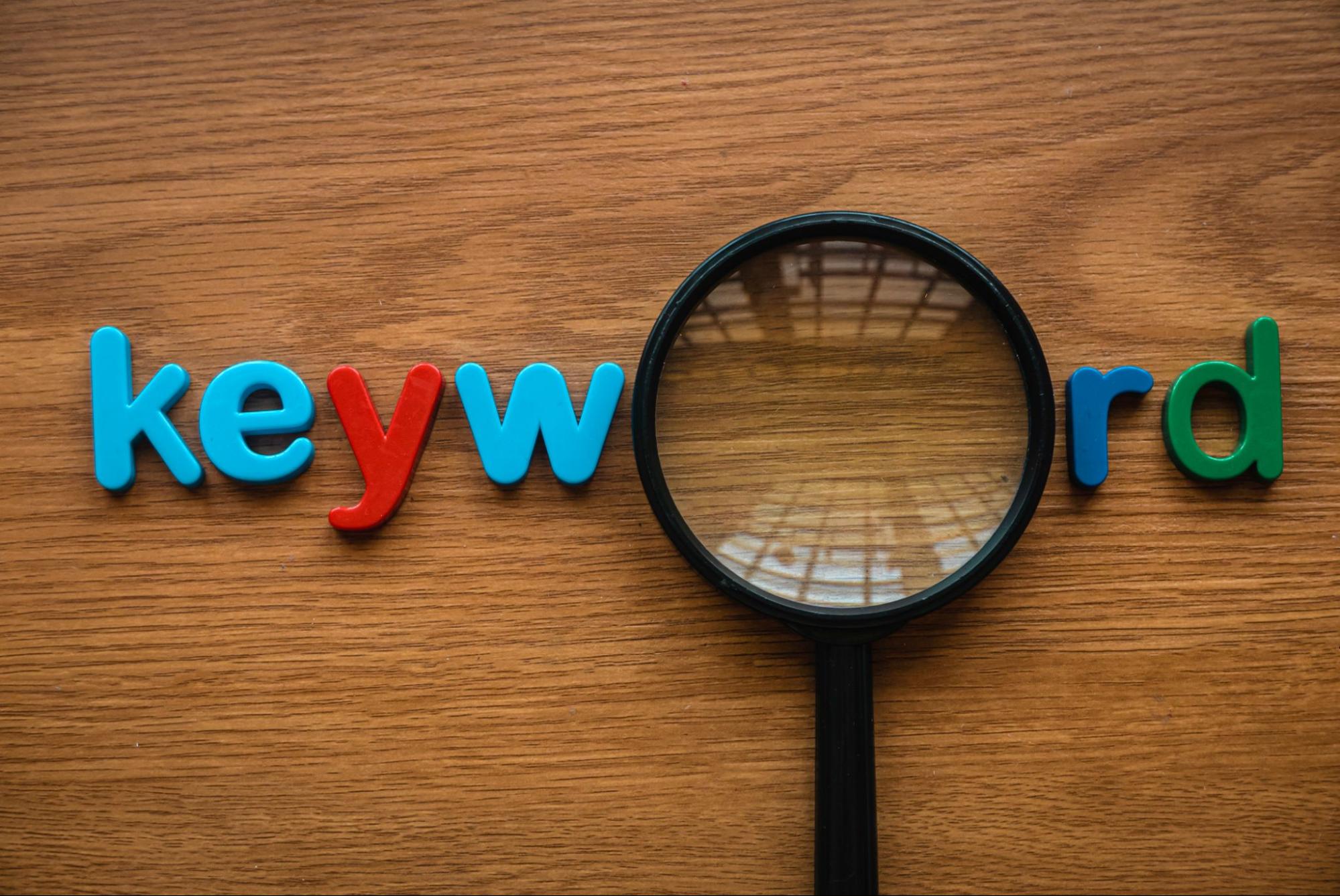 Colorful alphabet letters spelling out the word "keyword" with a magnifying glass in the place of the "O" on a wooden desk.