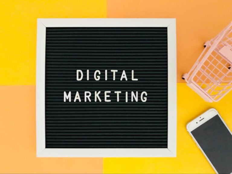 Words “digital marketing” on a letterboard with a toy shopping cart and a cell phone beside it.